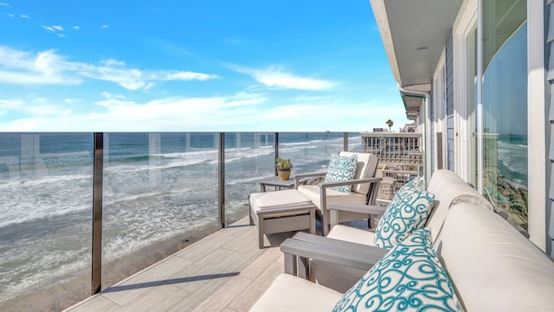 Un balcone con vista sull'oceano, arredato con un divano, poltrone e un piccolo tavolino con una pianta.