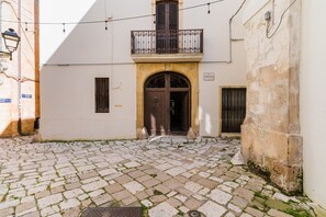 A cobblestone courtyard with a central entrance, a balcony with wrought iron railings, and a building with a stone facade.