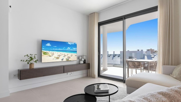 Un salon moderne doté d’un grand téléviseur, d’un canapé, d’une table basse et d’un balcon offrant une vue sur la ville.