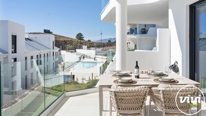 Un espace de restauration extérieur moderne, avec vue sur la piscine, une architecture blanche et des chaises en osier.