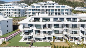 Un hôtel moderne à plusieurs étages, doté de balcons, d’une pelouse bien entretenue et surplombant un paysage montagneux.