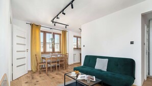 Een moderne woonkamer met een groene bank, een glazen salontafel en een eethoek met houten meubilair.