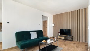 Een woonkamer met een donkergroene bank, een bijzettafeltje met croissants, een flatscreen televisie en een wand van houten latten.