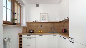 Een kleine keuken met witte kastjes, een houten aanrecht, een raam met een plant en een lijst aan de muur.