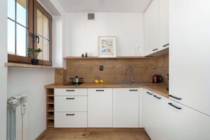Eine kleine Küche mit weißen Schränken, einer Holz Arbeitsplatte, einem Fenster mit Pflanze und einem gerahmten Bild an der Wand.