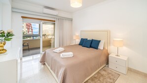 Hotelkamer met een bed, bedlampjes, een klein tafeltje, een stoel en uitzicht op het buiten.