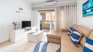 Een moderne woonkamer met een flatscreen-tv, een bank met gestreepte kussens, een witte console tafel en uitzicht door een glazen deur op een buitenbalkon.