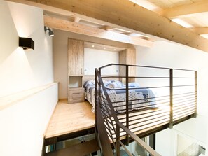 Et soveværelse med skunk, køjeseng, træbjælker, et lille skrivebord og en indbygget garderobe.