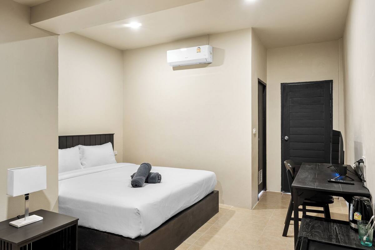 Una habitación de hotel con una cama, un escritorio, una silla, una lámpara y una puerta.