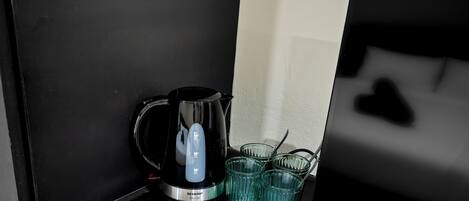 A black coffee maker and two clear glasses on a black countertop.