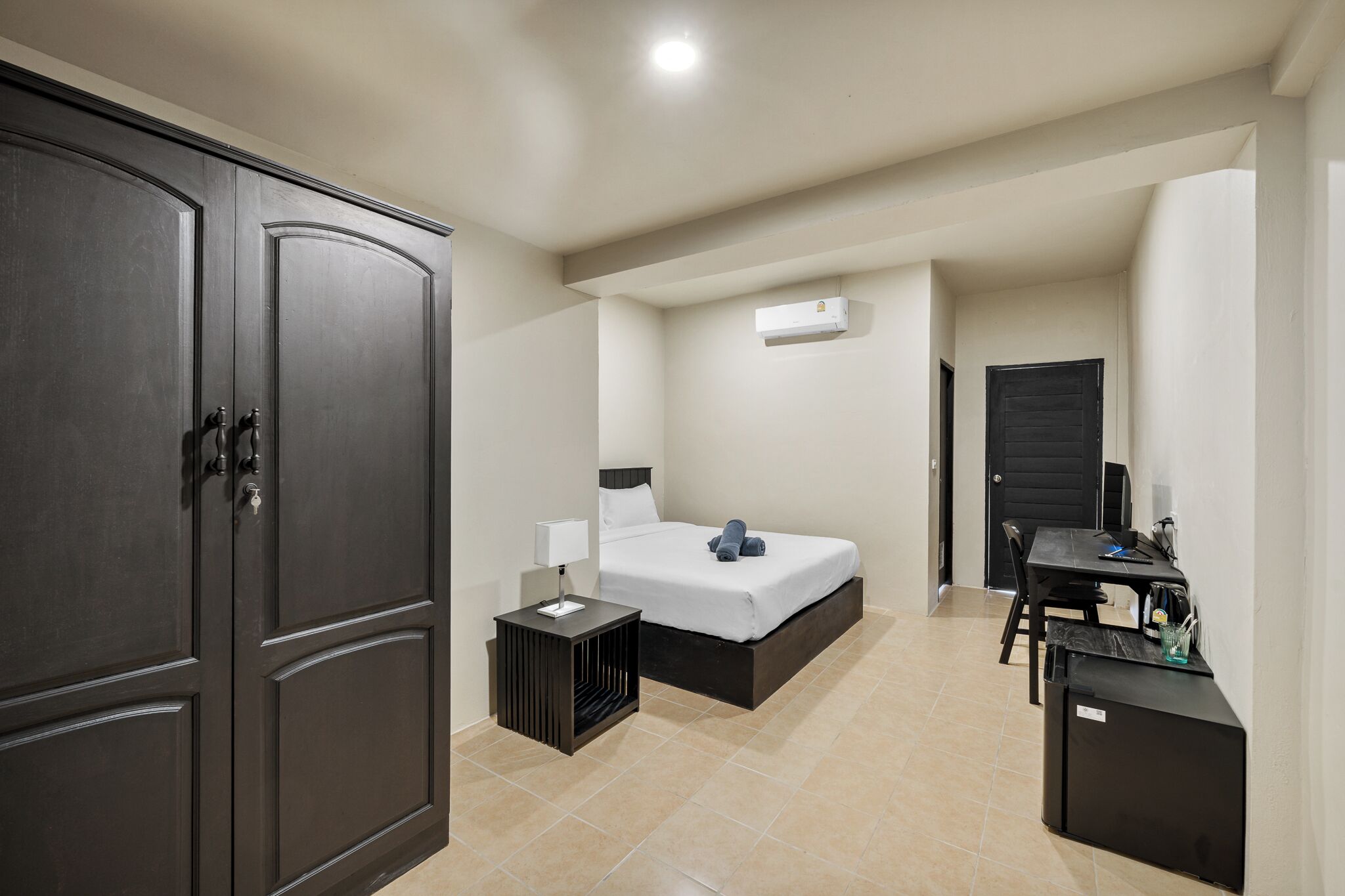 Quarto de hotel compacto com cama, mesa de cabeceira, guarda-roupa e uma pequena área de trabalho.