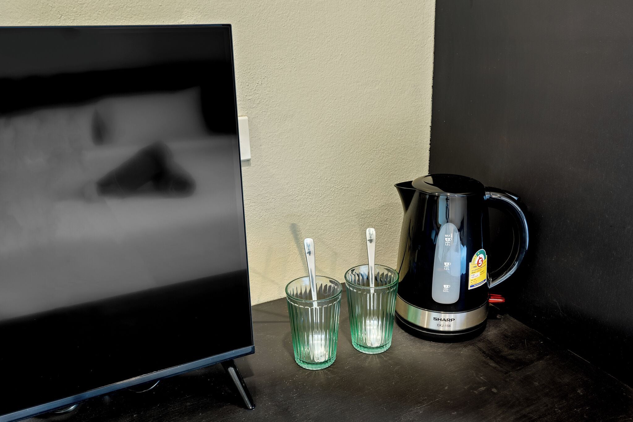 A coffee maker and two glasses on a table next to a television.