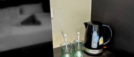 A coffee maker and two glasses on a table next to a television.