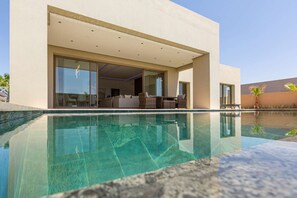 Una casa moderna amb una piscina d'infinity, grans portes de vidre que donen a una zona d'estar exterior, i una vista despejada de la piscina.