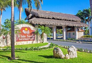 Ett semesterhotell som heter White Sands, med en byggnad med halmtak, palmer och en skylt som visar att det är ett hotell med golfbana och strand.