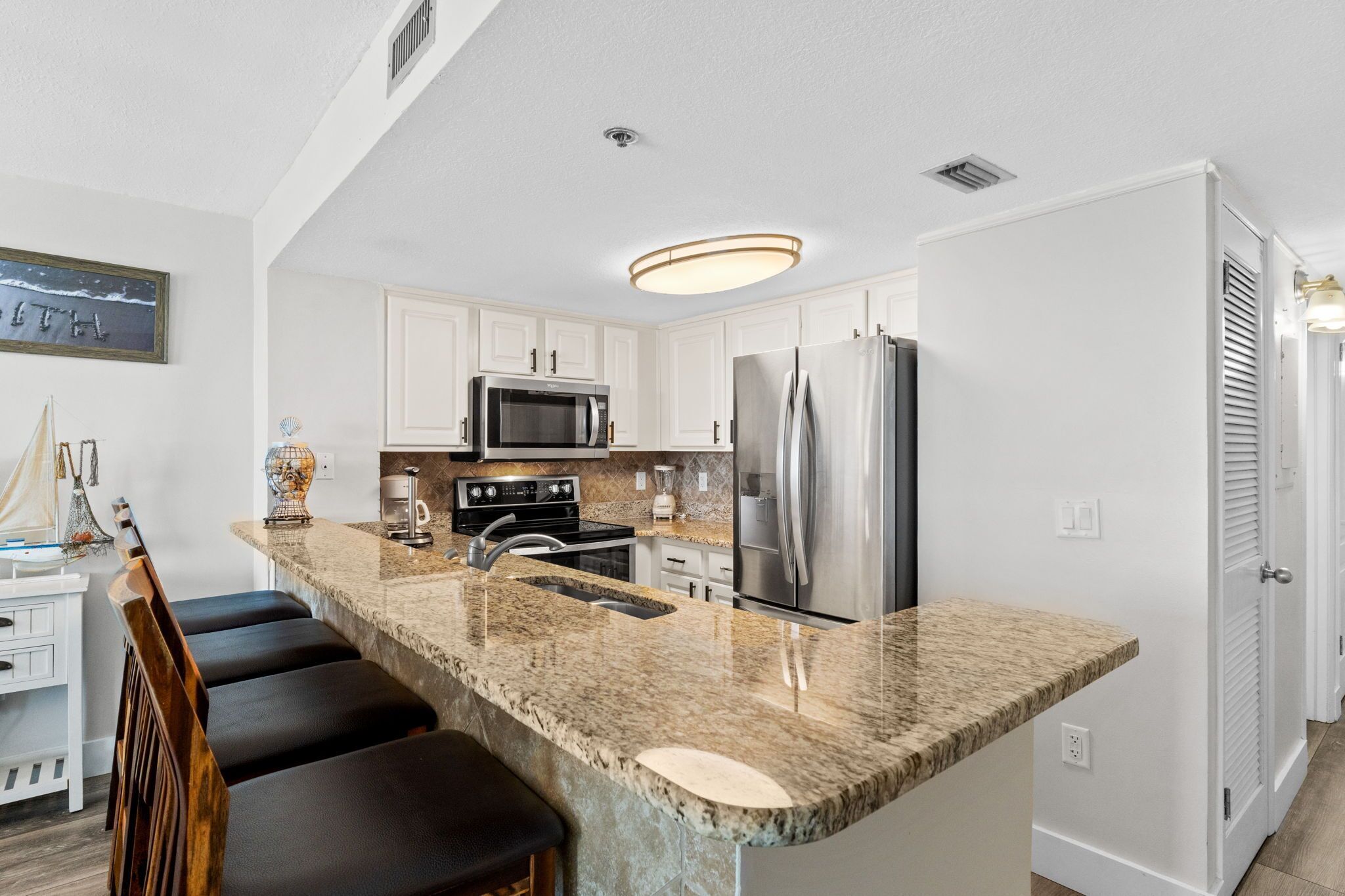A modern kitchen with granite countertops, stainless steel appliances, and a bar area with stools.