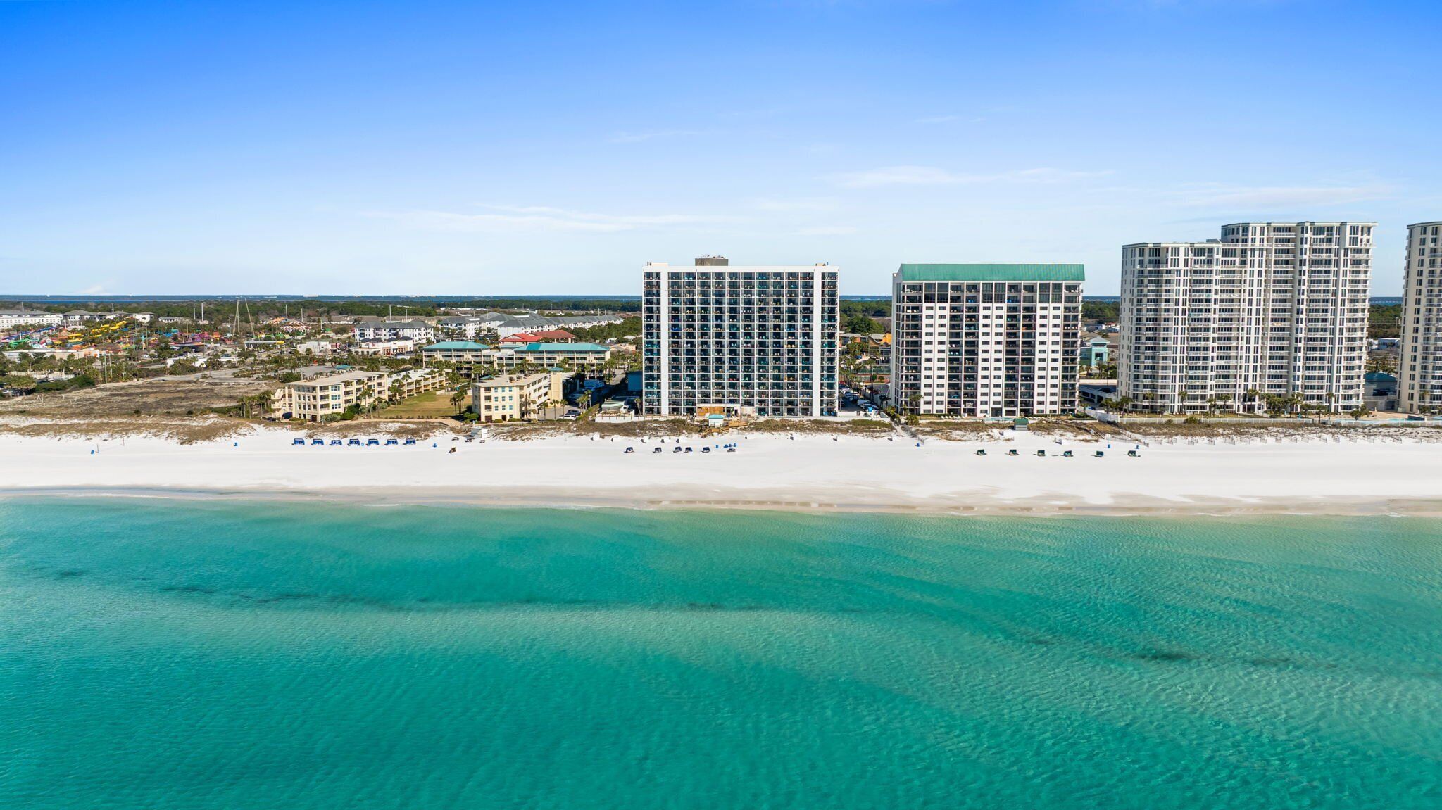 A coastal hotel area with multiple high-rise buildings, a sandy beach, and clear turquoise waters.