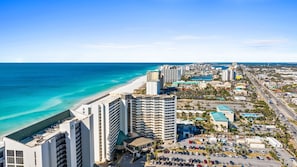 A coastal cityscape with a beachfront hotel, high-rise buildings, and a busy road. - SunDestin Gulf-View 1BR Condo | 8th Floor, Indoor/Outdoor Pools, Private Beach Access (Destin)