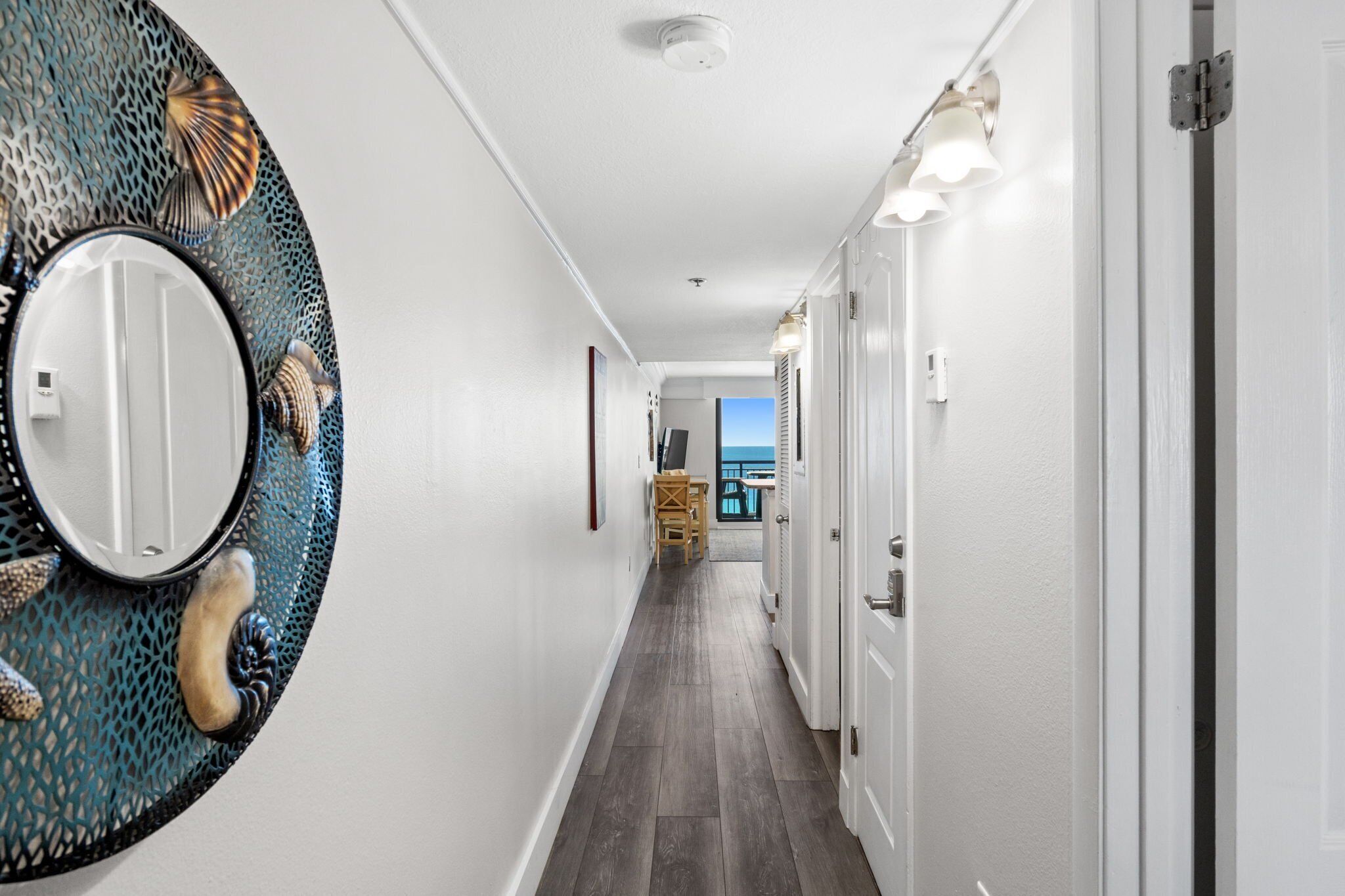 A hallway with a decorative wall piece, a door with a handle, and a view to a balcony.