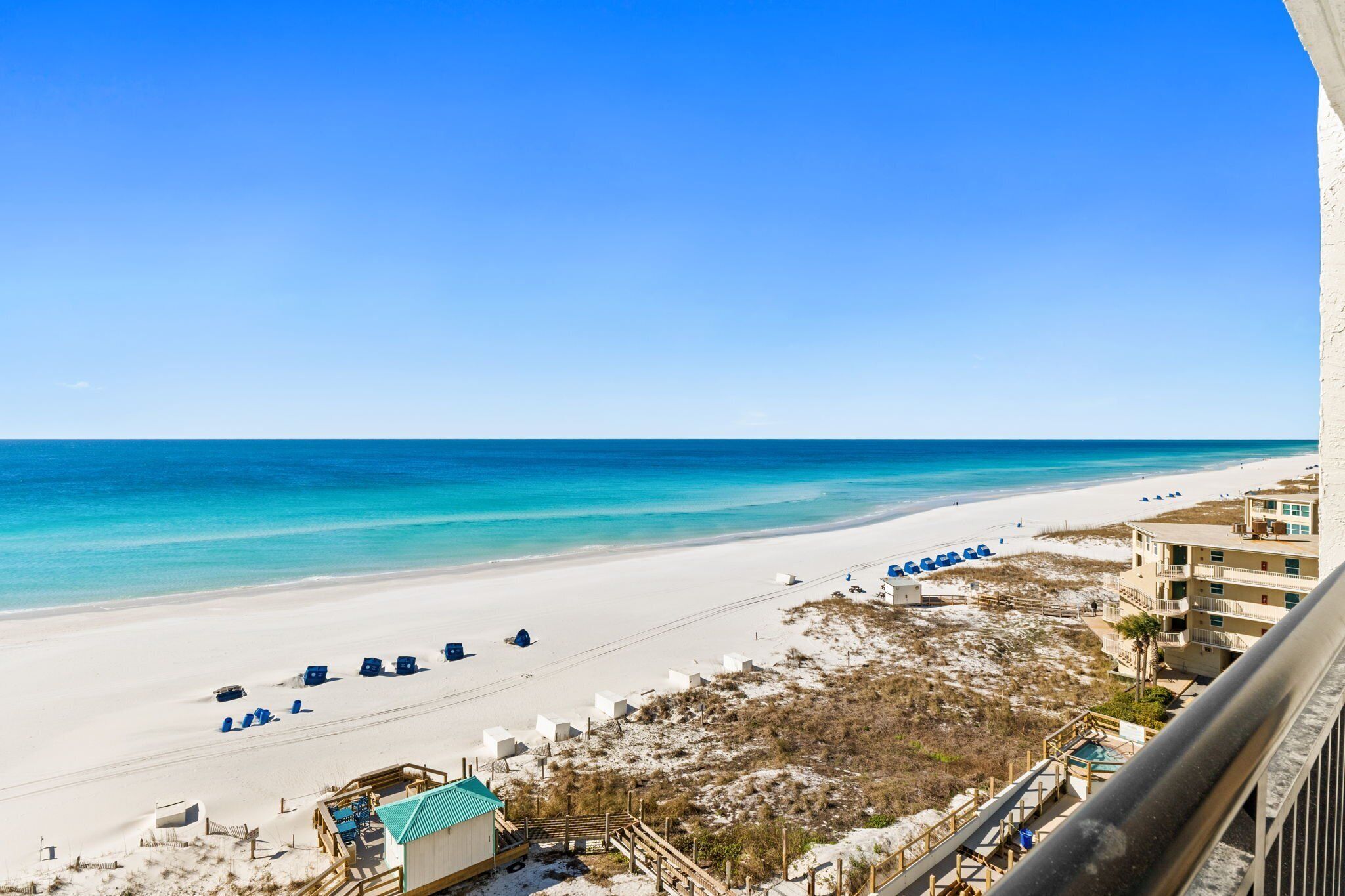 Ein Strand mit blauem Himmel, sandigem Ufer und einem Gebäude mit Balkon mit Blick auf den Strand.