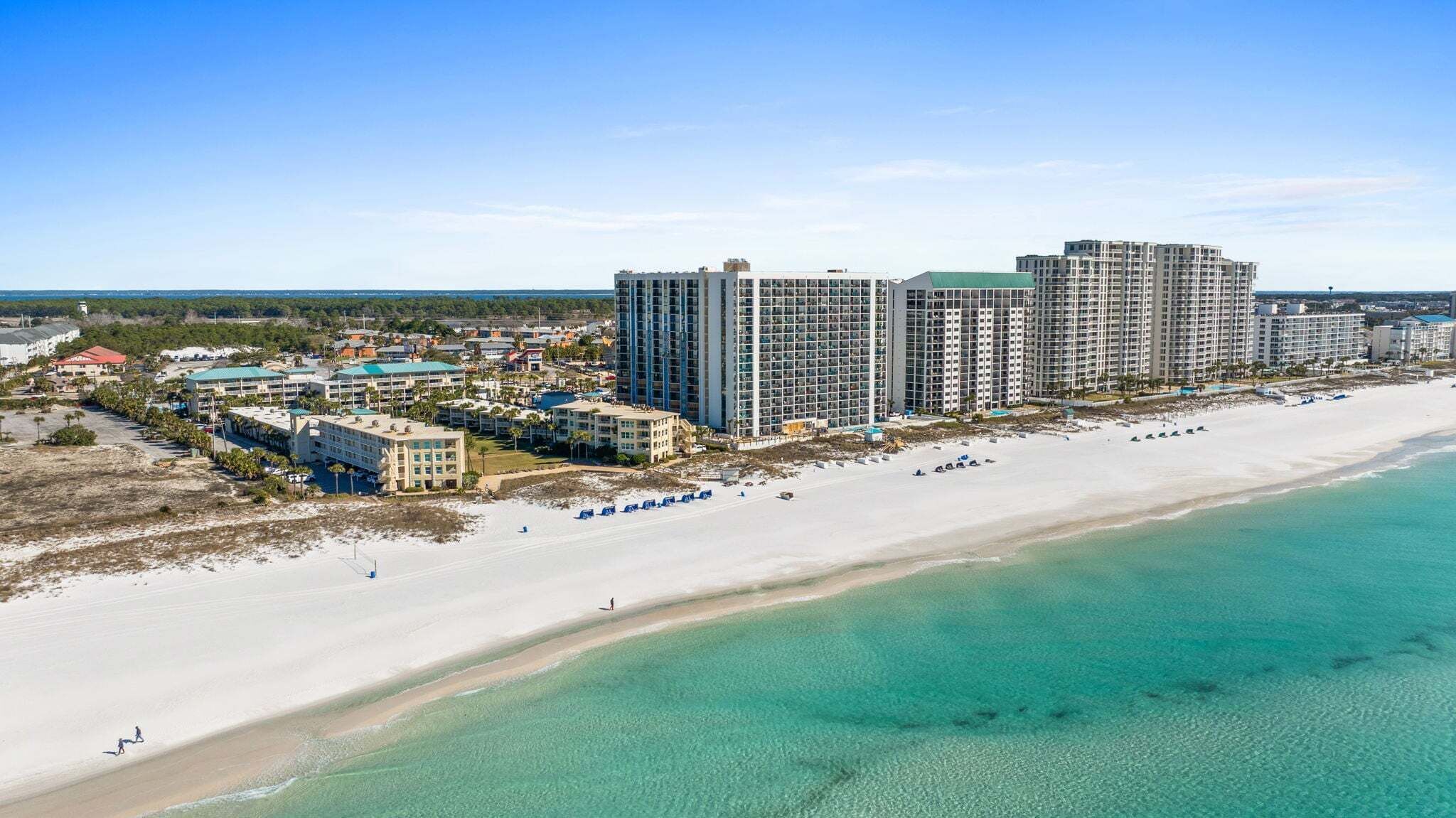 A coastal hotel with multiple high-rise buildings, a sandy beach, and clear turquoise waters.