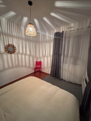 Ein Schlafzimmer mit einem Bett, einem roten Sessel, einer Pendelleuchte und einer Duschvorhang.