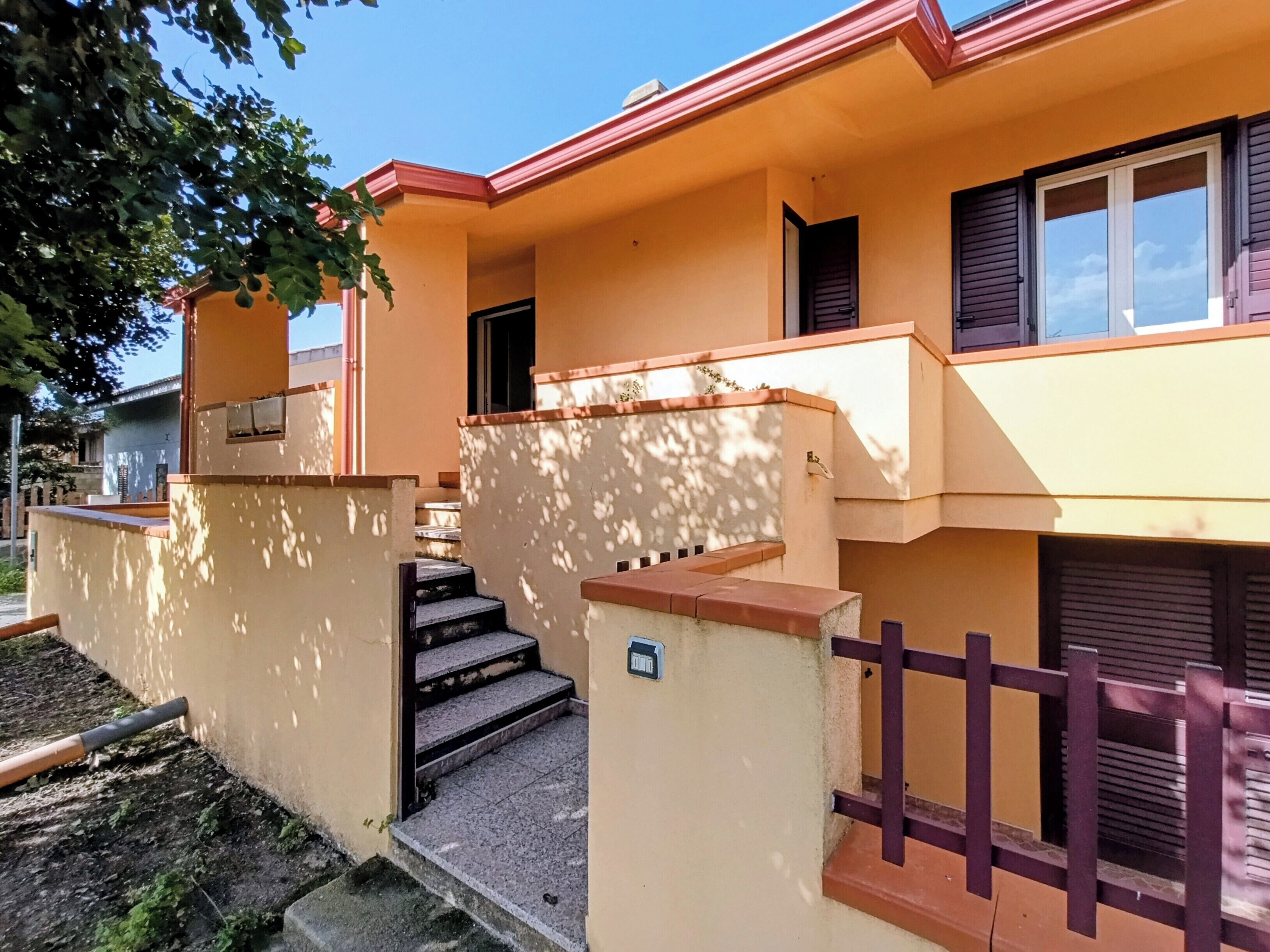 A two-story building with a red roof, a staircase leading to the entrance, and a small porch area.
