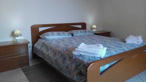 Ein ordentlich bezogenes Bett mit floralem Bettzeug, zwei Nachttischlampen und ein Stapel Handtücher auf dem Nachttisch.