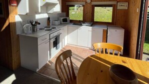 Una cocina pequeña con armarios blancos, una estufa y un lavabo. Hay una mesa de madera con un bol y una silla.