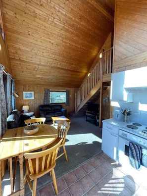 L’intérieur chaleureux d’un chalet comprend une table à manger en bois, des chaises, un canapé et un coin cuisine avec une cuisinière et un évier.