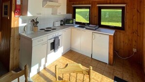 Una cucina compatta con soffitto in legno, mobili bianchi, un forno a microonde e una finestra con vista sull'esterno.