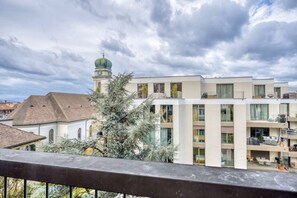 Un bâtiment moderne, avec une église traditionnelle en arrière-plan, dont le clocher, surmonté d’un dôme vert, est particulièrement imposant.