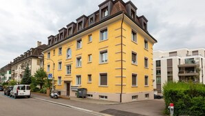 A multi-story residential building with a yellow facade, multiple windows, and a visible entrance.