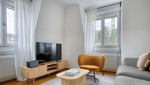 A modern living room with a flat-screen TV on a wooden stand, a round wooden coffee table, a mustard-colored armchair, and a grey sofa.