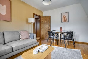 Un salon avec un canapé gris, une table basse en bois et un coin repas comprenant une table ronde et des chaises noires.