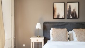 Una habitación de hotel con cama, mesita de noche, lámpara y dos obras de arte en la pared.
