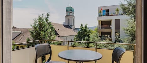 A balcony with two chairs and a table, overlooking a building with a clock tower.