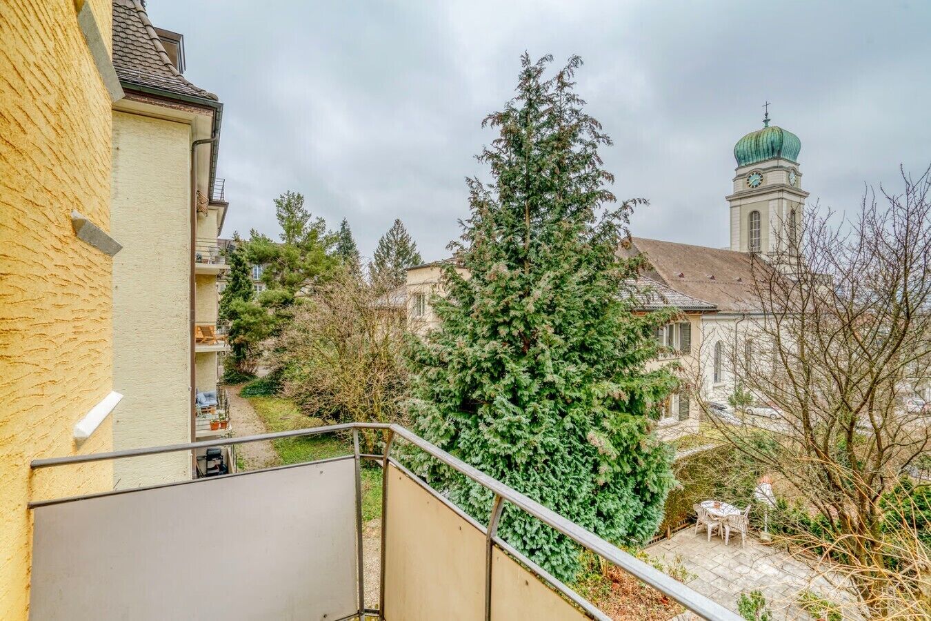 Un quartiere residenziale con una scala, un grande albero sempreverde e una chiesa con una cupola verde sullo sfondo.