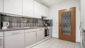 A modern kitchen with white cabinets, a stainless steel kettle, and a wood-framed door.