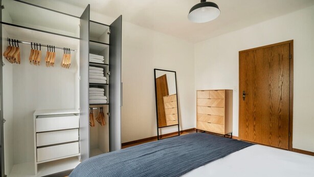 A bedroom with a bed, a wardrobe, a mirror, and a wooden door.