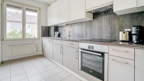 A modern kitchen with white cabinets, a Bosch oven, a coffee maker, and a window with blinds.