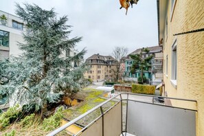 A residential area with a balcony overlooking a courtyard with a large evergreen tree and a small white vehicle. - 3-BR in Wipkingen · parking · tram nearby (Zürich)