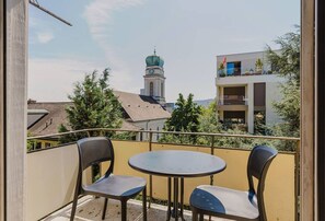 Un balcon avec deux chaises et une petite table, d’où l’on peut admirer un bâtiment doté d’une tour horlogère et d’une architecture moderne.