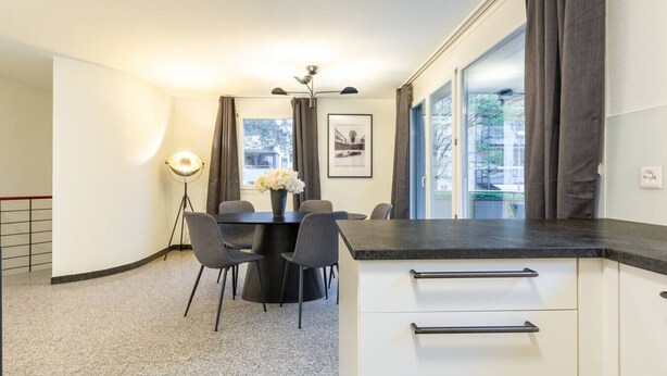 A modern kitchen with a dining area, featuring a black countertop, white cabinets, and a vase with flowers on the table.