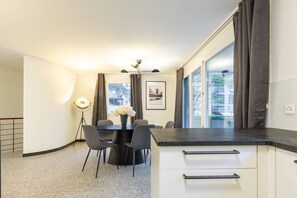 A modern kitchen with a dining area, featuring a black countertop, white cabinets, and a vase with flowers on the table.