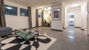 A modern living room with a glass coffee table, a grey sofa, and a patterned rug.