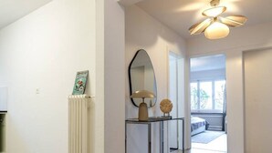 Um interior moderno com piso de madeira, ventilador de teto e corredor que leva a um quarto.