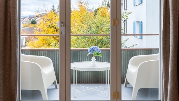 Quarto com porta de correr de vidro que dá para uma varanda externa com mesa e cadeiras.