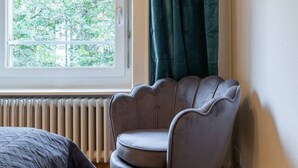 Une chambre moderne avec un fauteuil gris, une fenêtre donnant sur des arbres et un radiateur.
