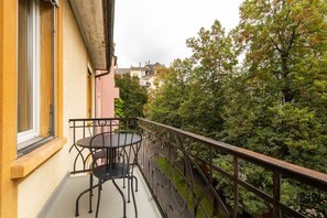 Un balcón con mesa y sillas, con vistas a un jardín y edificios.